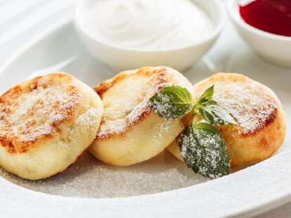 Cheesecake, fresh jam and mint. Cottage cheese pancakes or curd fritters decorated powdered sugar in plate close view. Healthy and diet breakfast