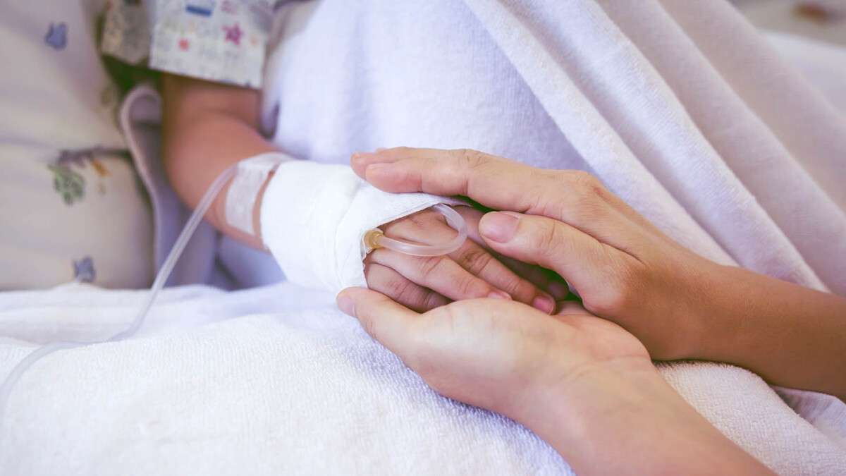 Close up hand of parent holding child's hand in hospital.