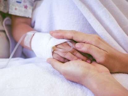 Close up hand of parent holding child's hand in hospital.