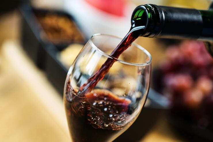 Red wine pouring into a wine glass at a tasting with various types of appetizers.