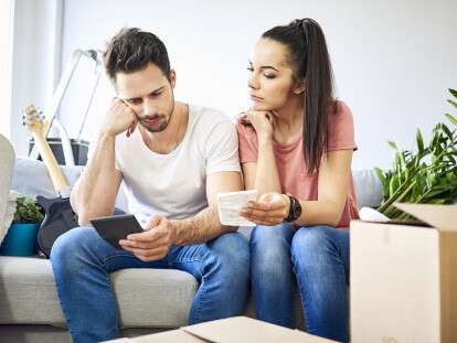 Serious couple sitting on couch in new home checking bills