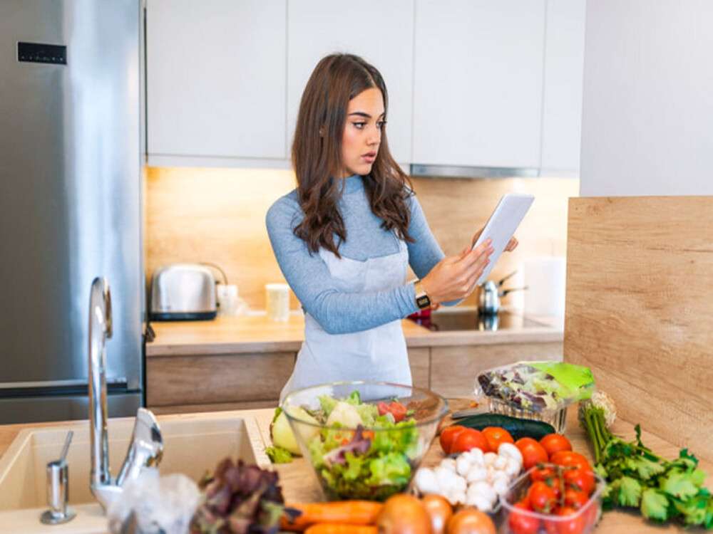 Woman In Kitchen Following Recipe On Digital Tablet