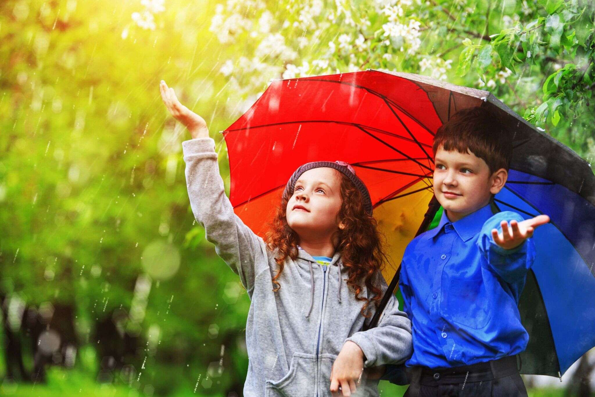 Children under umbrella enjoy to spring rain outdoors.