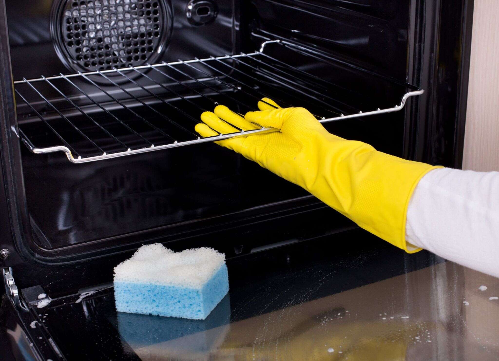 50443286 - close up of female hand with yellow protective gloves cleaning oven