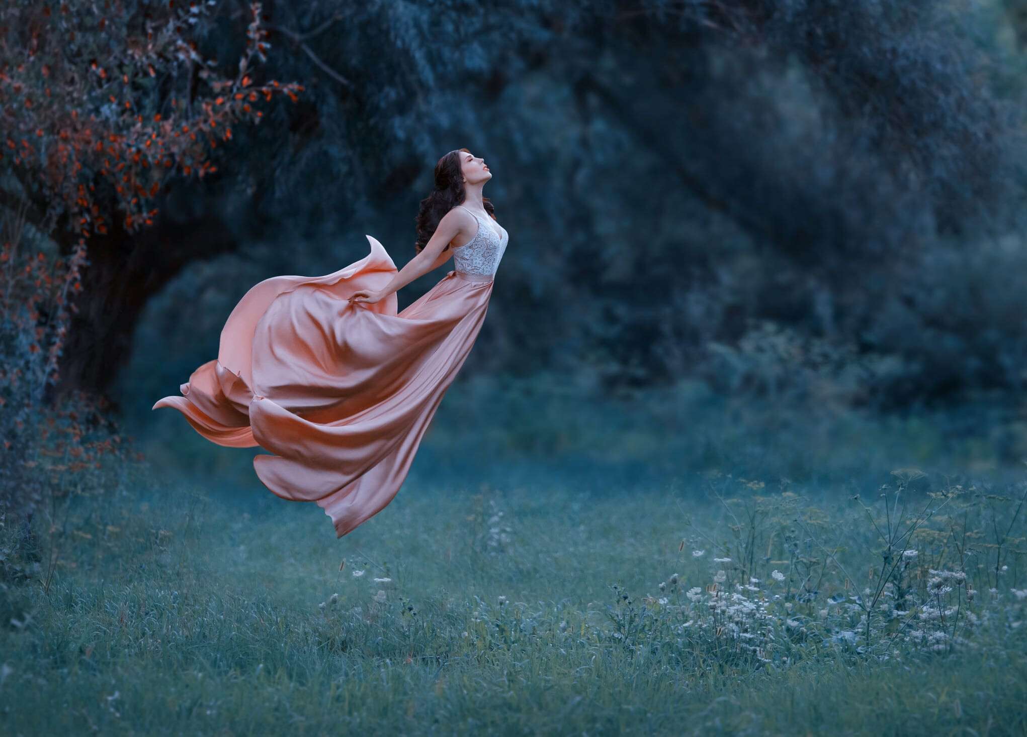 A young woman, a mysterious witch is floating in the air like a butterfly. A luxurious, long dress waving in the wind. Cold forest background. Enchanted princess. Art photo of levitation